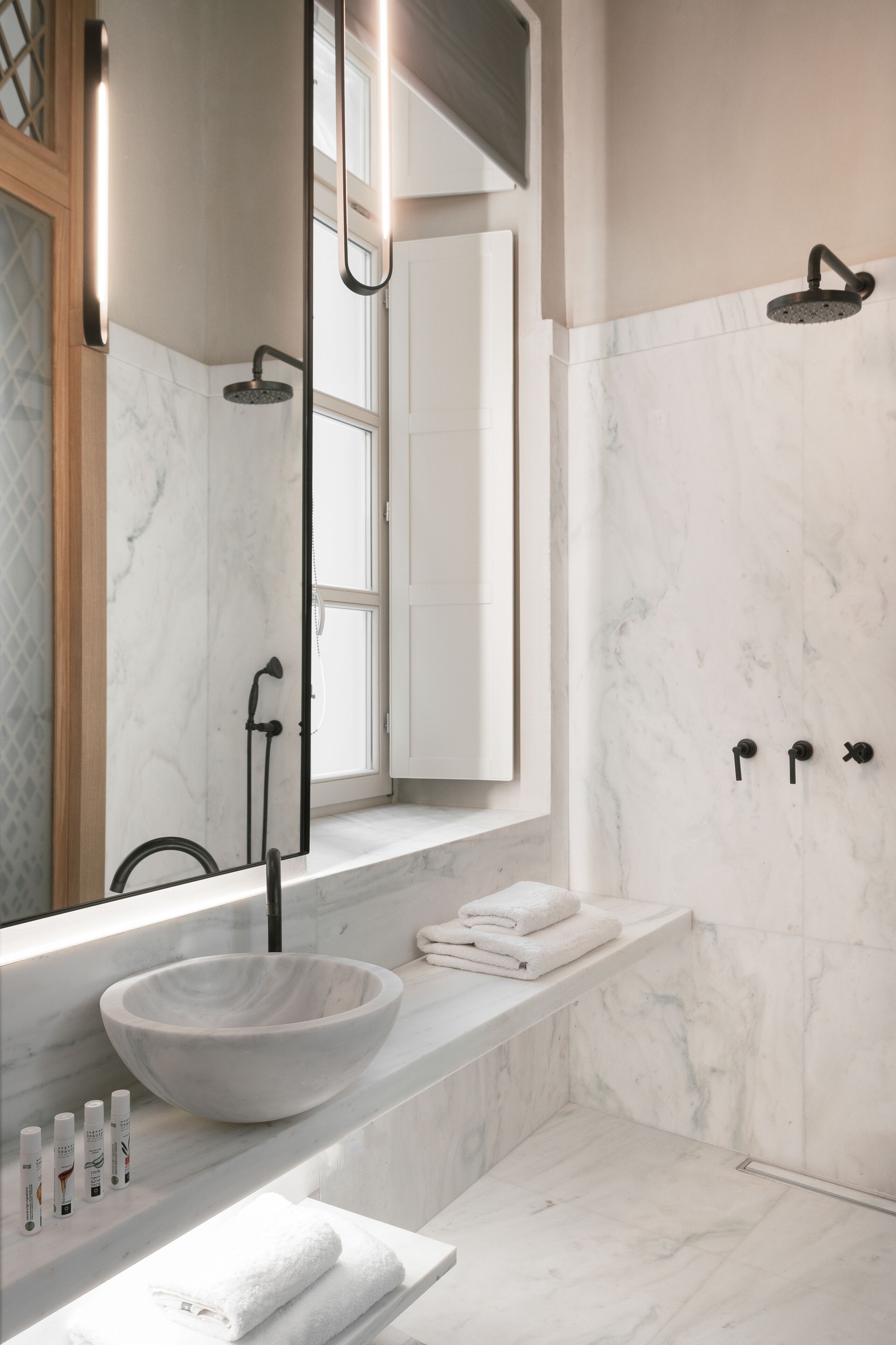 A modern bathroom with a large marble sink, a mirror, a shower, and a towel rack.