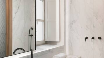 A modern bathroom with a large marble sink, a mirror, a shower, and a towel rack.