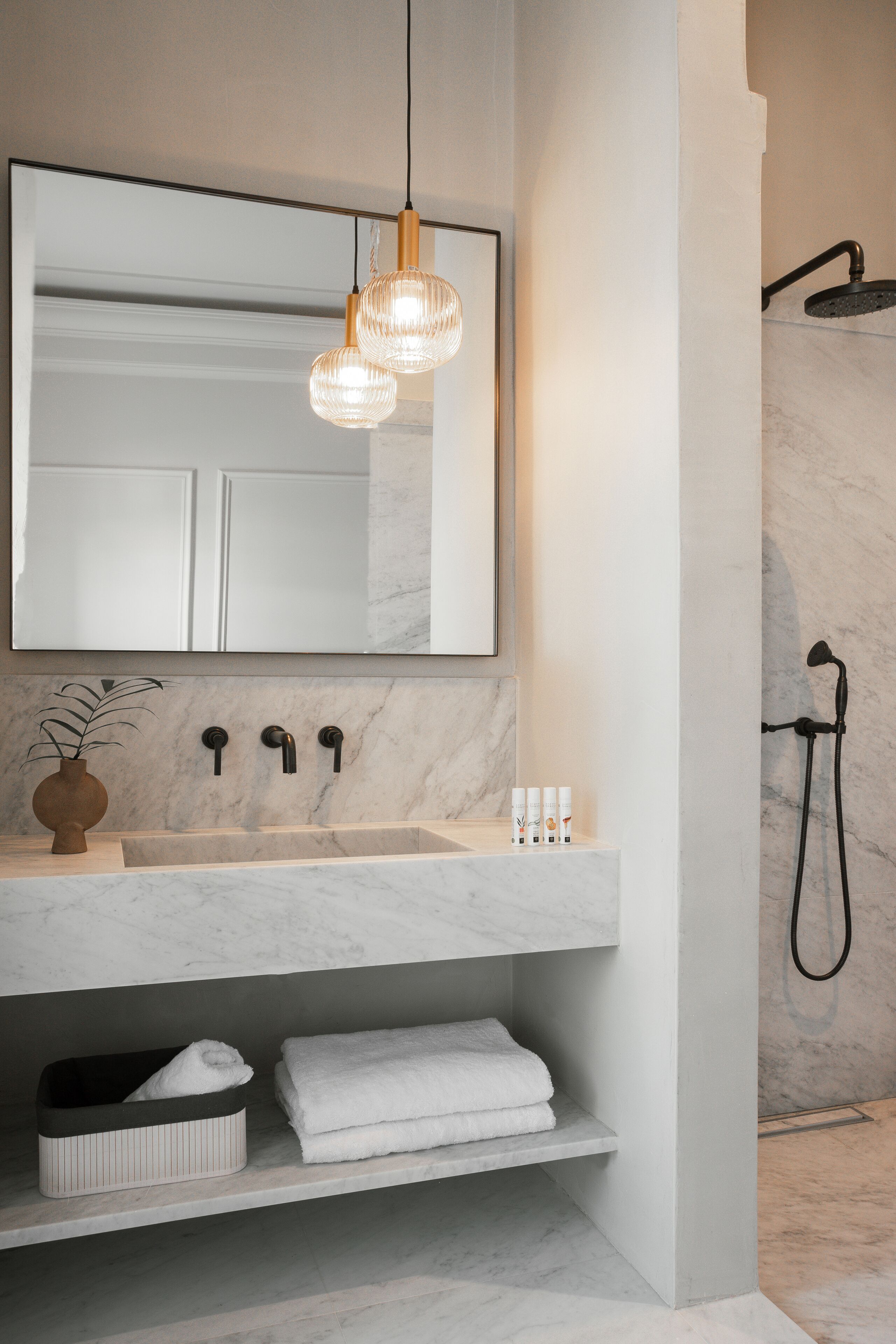 A bathroom with a marble sink, a mirror, a towel rack, and a shower.