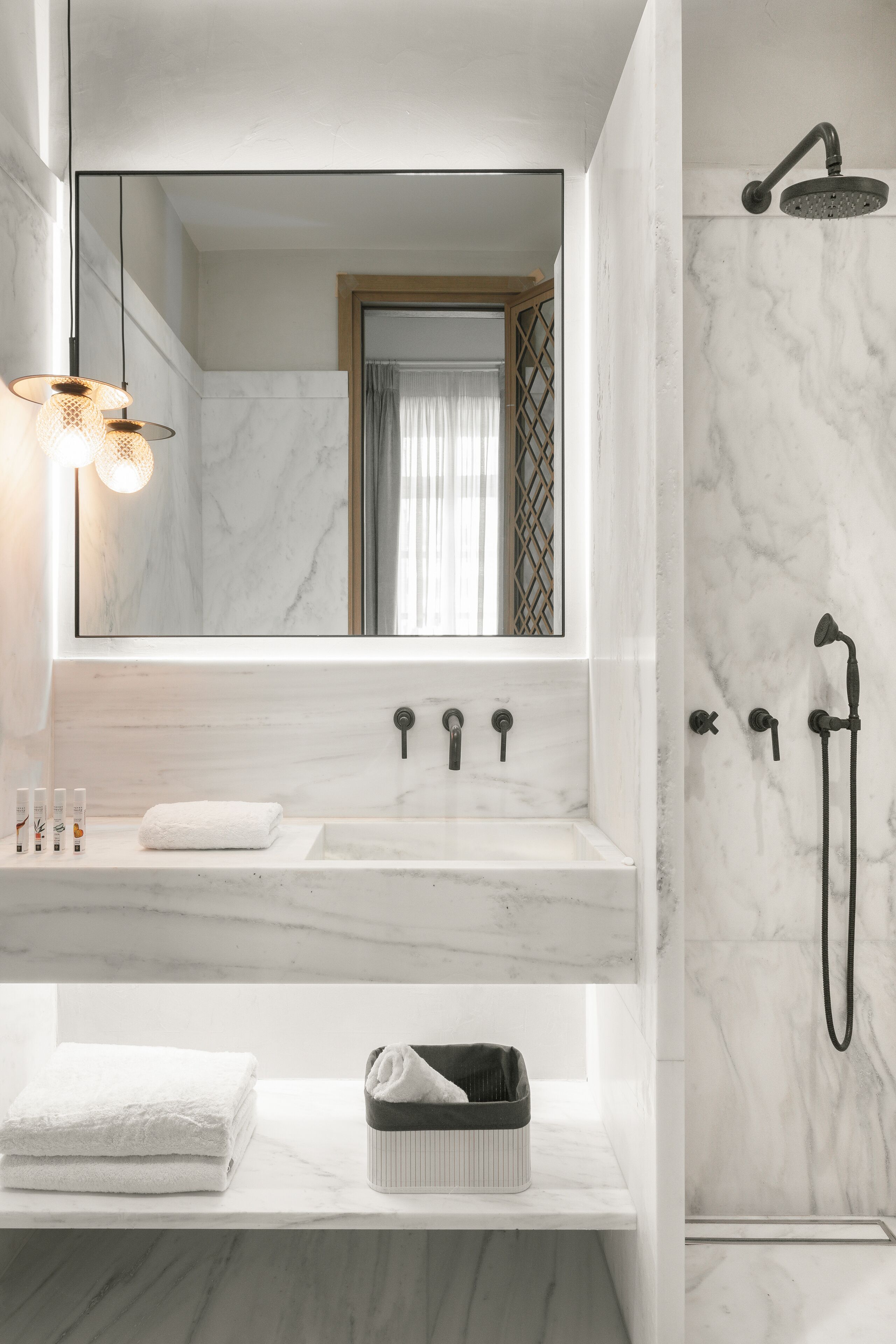 Un baño moderno con lavamanos de mármol, un espejo grande, ducha con cabezal de ducha de mano y un perchero para toallas.