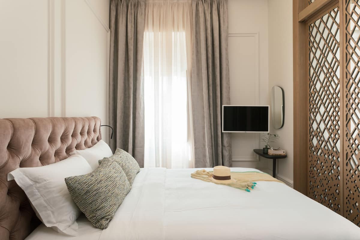 A neatly made bed with a tufted headboard, a television on a small table beside the bed, and a wooden partition with a lattice design.