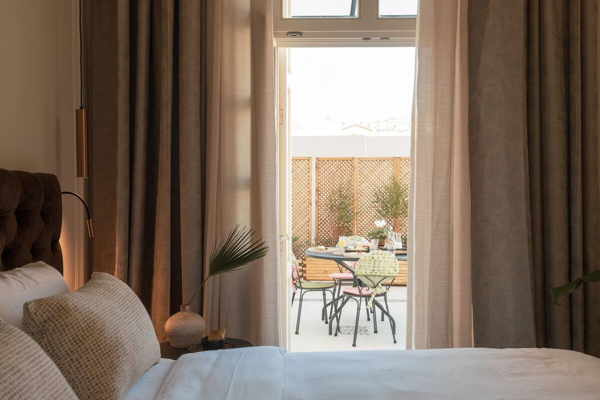 A bedroom with a bed, curtains, and a view of an outdoor dining area.