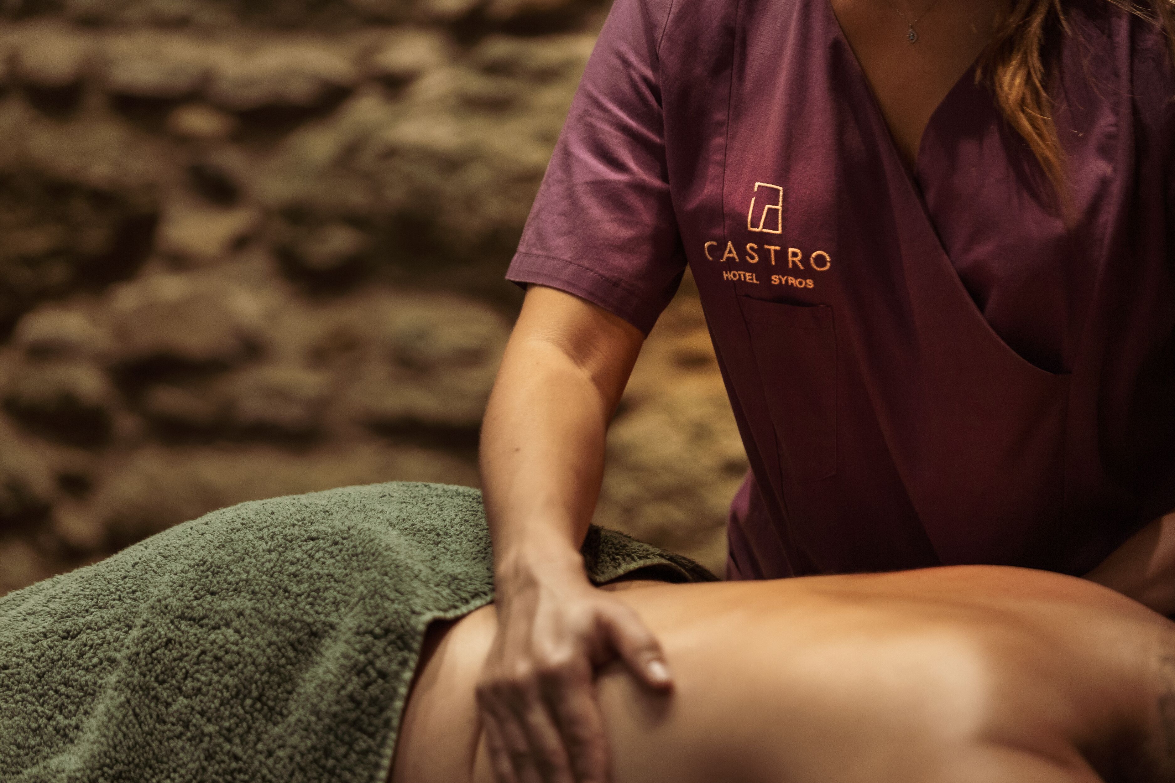 A person receiving a massage in a room with a stone wall background.