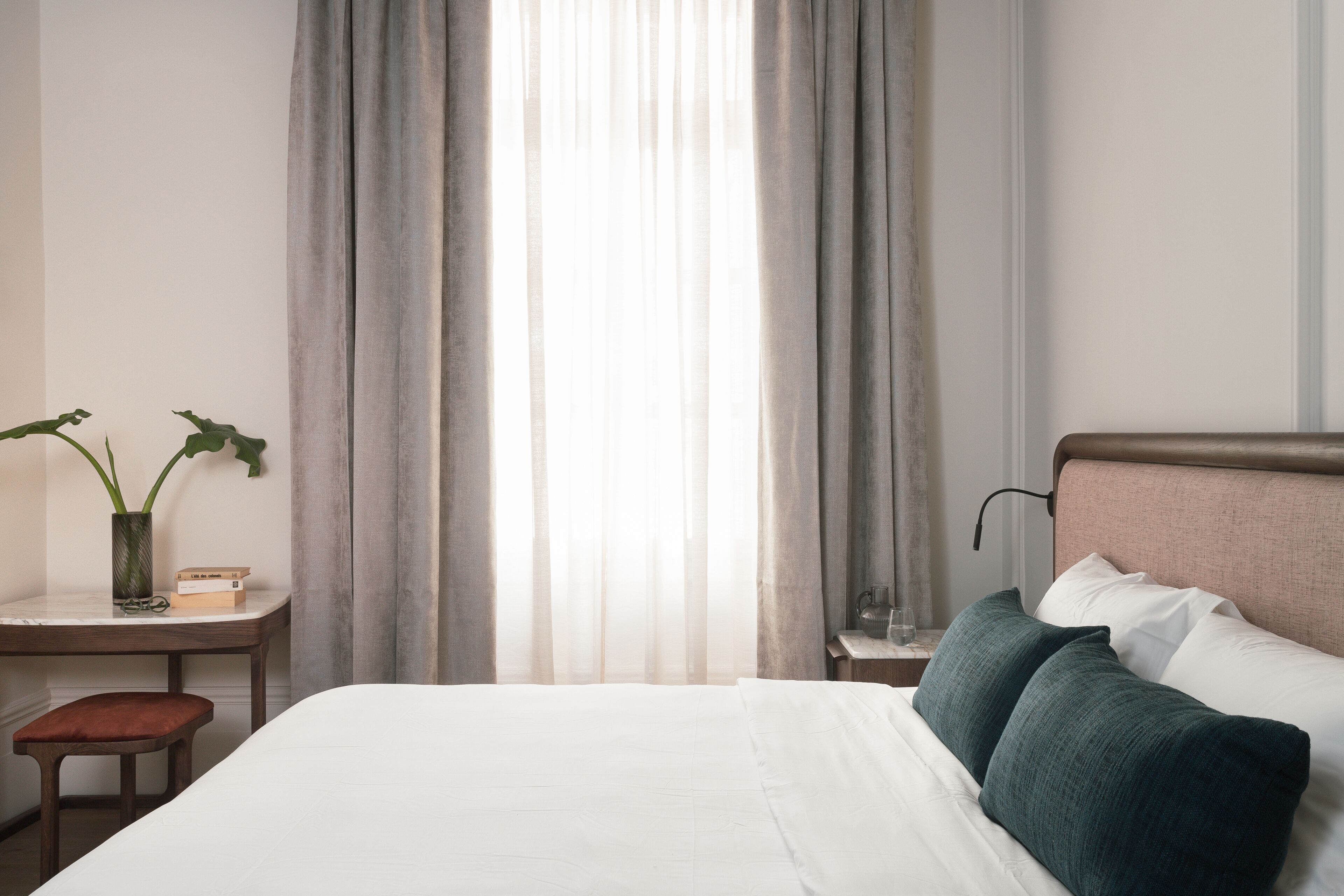 A hotel room with a bed, a desk, a chair, and a window with curtains.