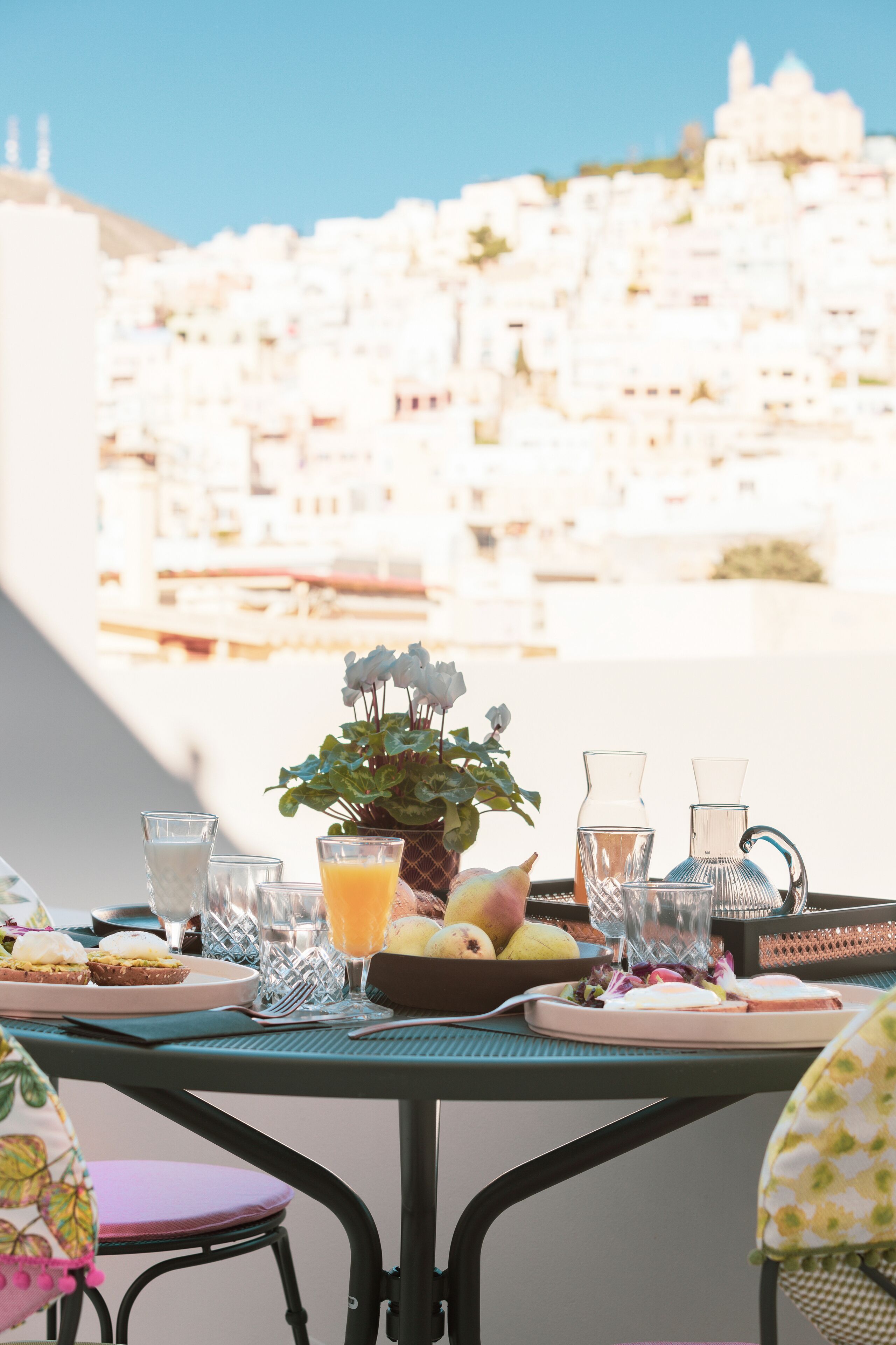 Una tavola imbandita con prodotti per la colazione, tra cui frutta, una caraffa e bicchieri, con vista sulla città sullo sfondo.
