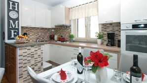 A modern kitchen with white cabinets, a tiled backsplash, a dining area with a table set for two, and a clock on the wall. - House 2087/39057 (Istria - Vinkuran), 500m from the beach (Vinkuran)