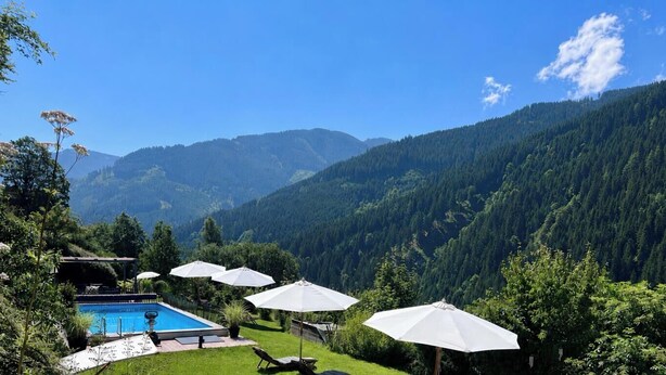 A pool with umbrellas, a lawn chair, and a mountain view. - ALM SEASONS - Family Chalet-Studio with sauna (Saalbach)