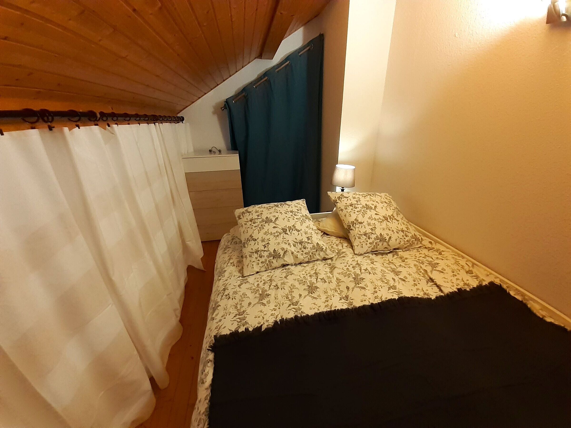 Un dormitorio con cama, mesita de noche, lámpara y ventana con cortinas.