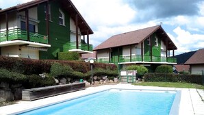 A swimming pool with a tiled deck, surrounded by green buildings with balconies and a stone wall. - Cozy chalet in Gérardmer, ski view, 4 guests (Gérardmer)