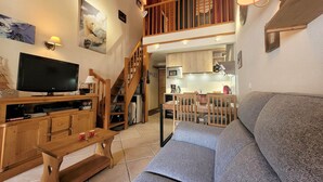 Una sala de estar acogedora con un sofá gris, un mueble de televisión de madera y una escalera de madera que sube a un nivel superior.