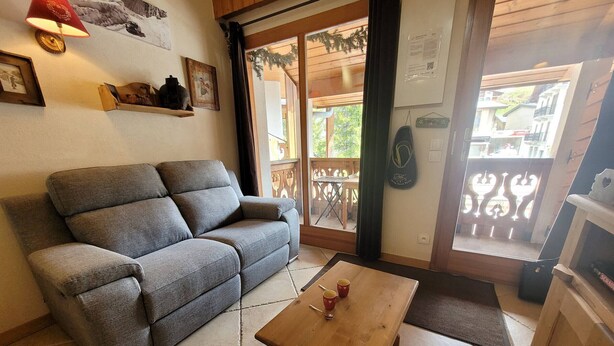 Un espacio de sala acogedor con un sofá gris, una mesa de centro de madera y vistas a un balcón con mobiliario exterior.