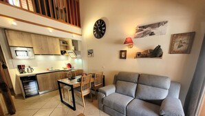 Un espacio habitable compacto con kitchenette, un sofá gris, una mesa de comedor de madera y una pequeña mesa de centro.