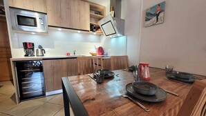 Una cocina moderna con armarios de madera, un microondas integrado y un comedor con una mesa de madera dispuesta para dos personas.