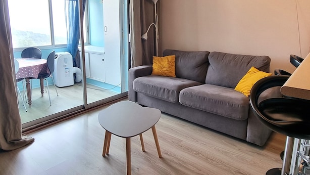 Ein Wohnzimmer mit grauem Sofa, einem kleinen weißen Tisch und einer Stehlampe.