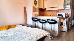 Ein kompaktes Hotelzimmer mit Bett, einer kleinen Küchenzeile, einer Waschmaschine und einer Bar mit Sitzgelegenheiten.