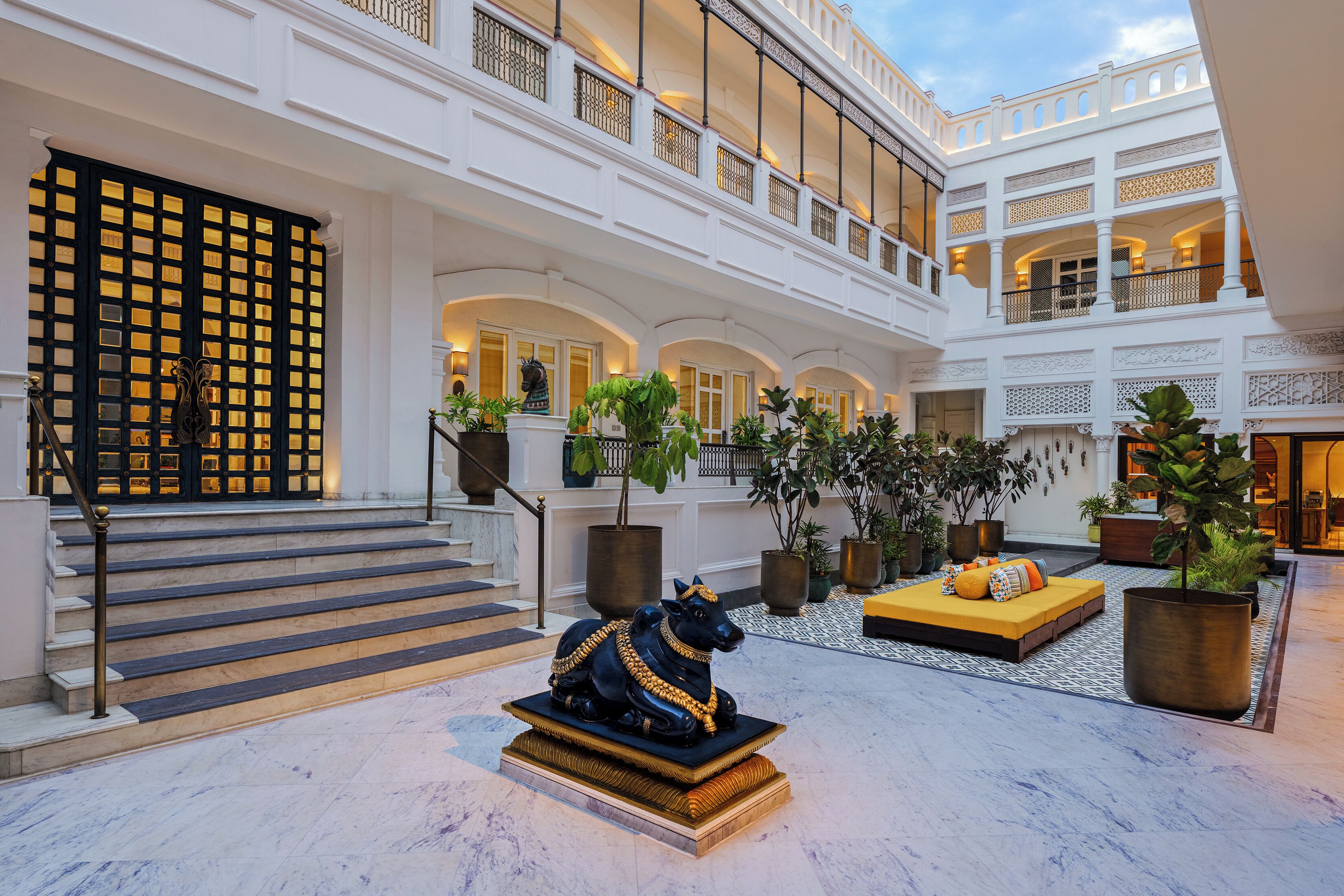 A spacious atrium with a grand staircase, a decorative black statue, and a seating area with cushions.
