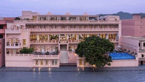 Hotel de vários andares com varandas, piscina e escadaria que dá acesso aos pisos superiores.