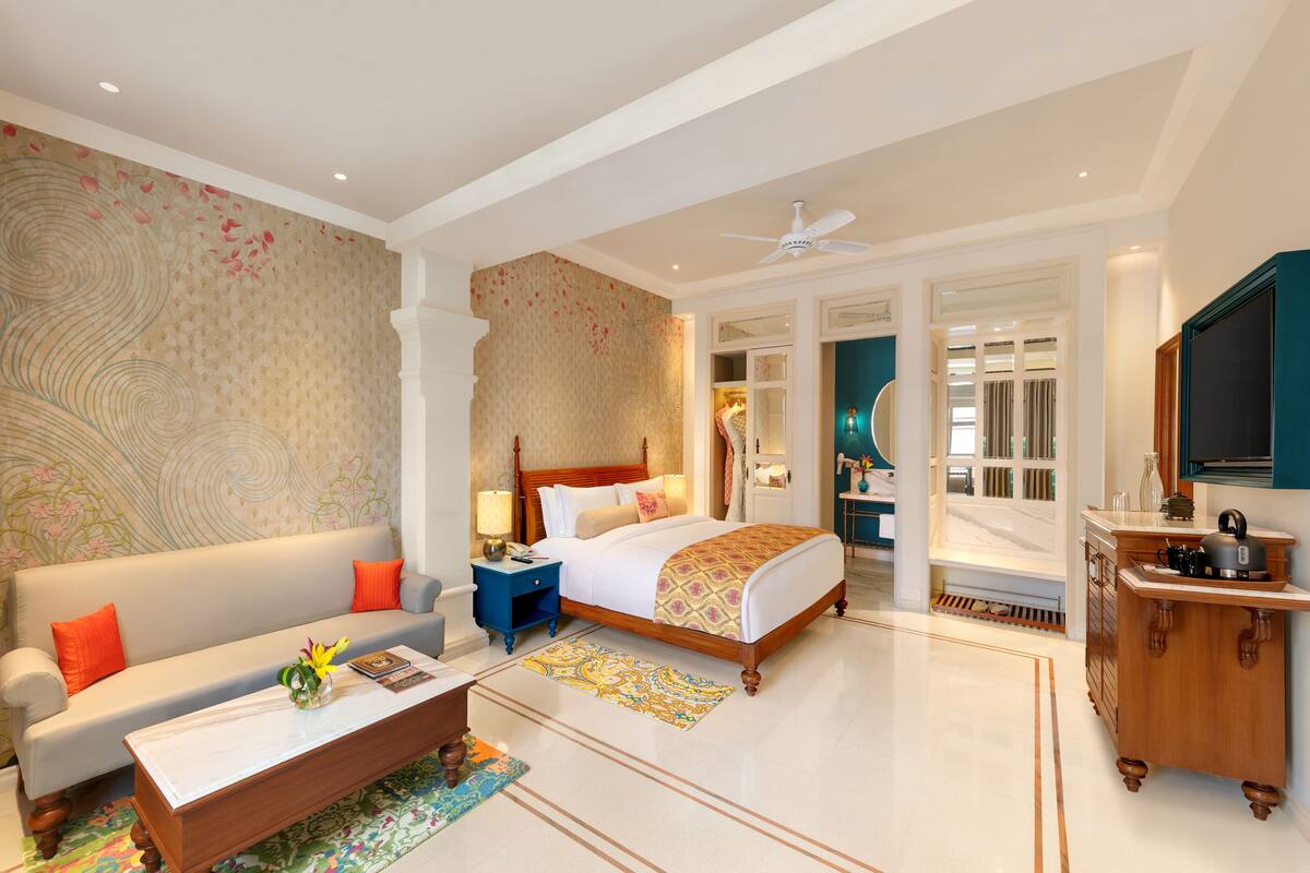 A spacious hotel room with a large bed, a sofa, a coffee table, and a TV.