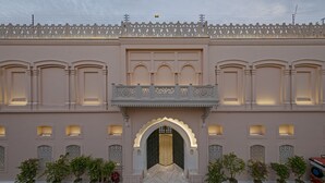 Um edifício com uma grande entrada em arco, várias varandas e plantas em vasos.
