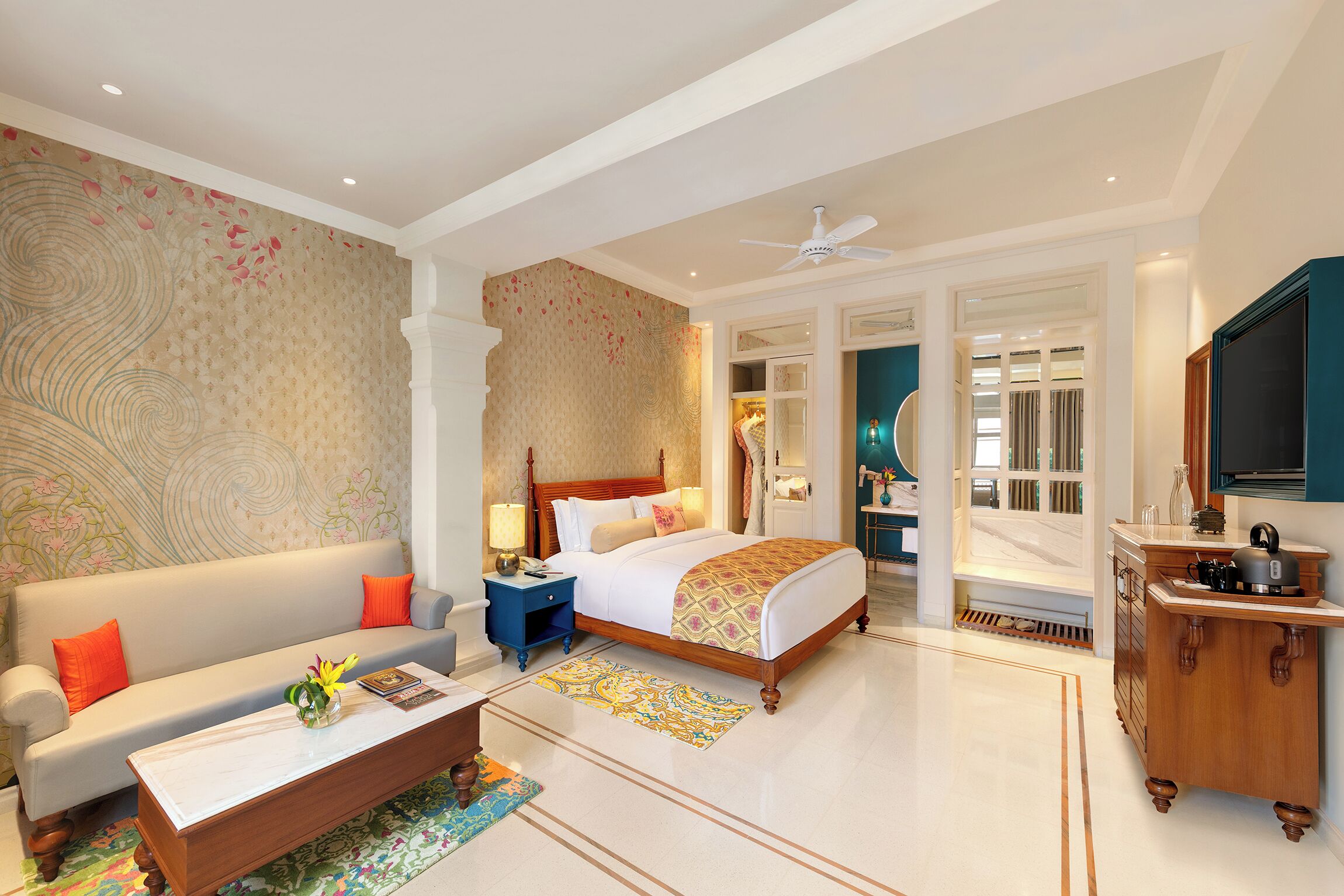 A hotel room with a bed, a sofa, a coffee table, a TV, and a bathroom visible through an open door.