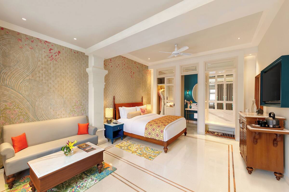A hotel room with a bed, a sofa, a coffee table, a TV, and a bathroom visible through an open door.