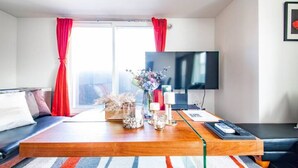 Un salon moderne avec un canapé, une table basse, un téléviseur et une fenêtre ornée de rideaux rouges.