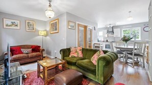 Ein Wohnzimmer mit einem grünen Sofa, einem braunen Ledersofa und einem Couchtisch aus Holz. Es gibt einen Fernseher, eine Lampe und einen roten Teppich.