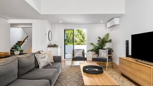 A modern living room with a grey sofa, two armchairs, a coffee table, a TV, and a large window with a view of greenery.