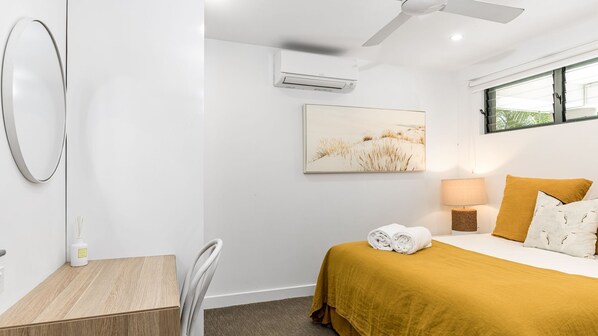 A hotel room with a bed, a desk, a chair, a ceiling fan, an air conditioner, a window, and a painting on the wall. - Lawson House 2 - Beautiful Byron Beachfront in the Centre of Town (Byron Bay)