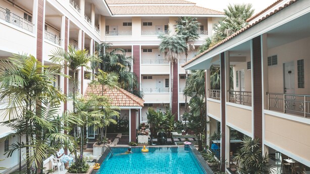 A multi-level hotel with a central swimming pool surrounded by lush greenery and palm trees. - Nattida Place (Chiang Mai)