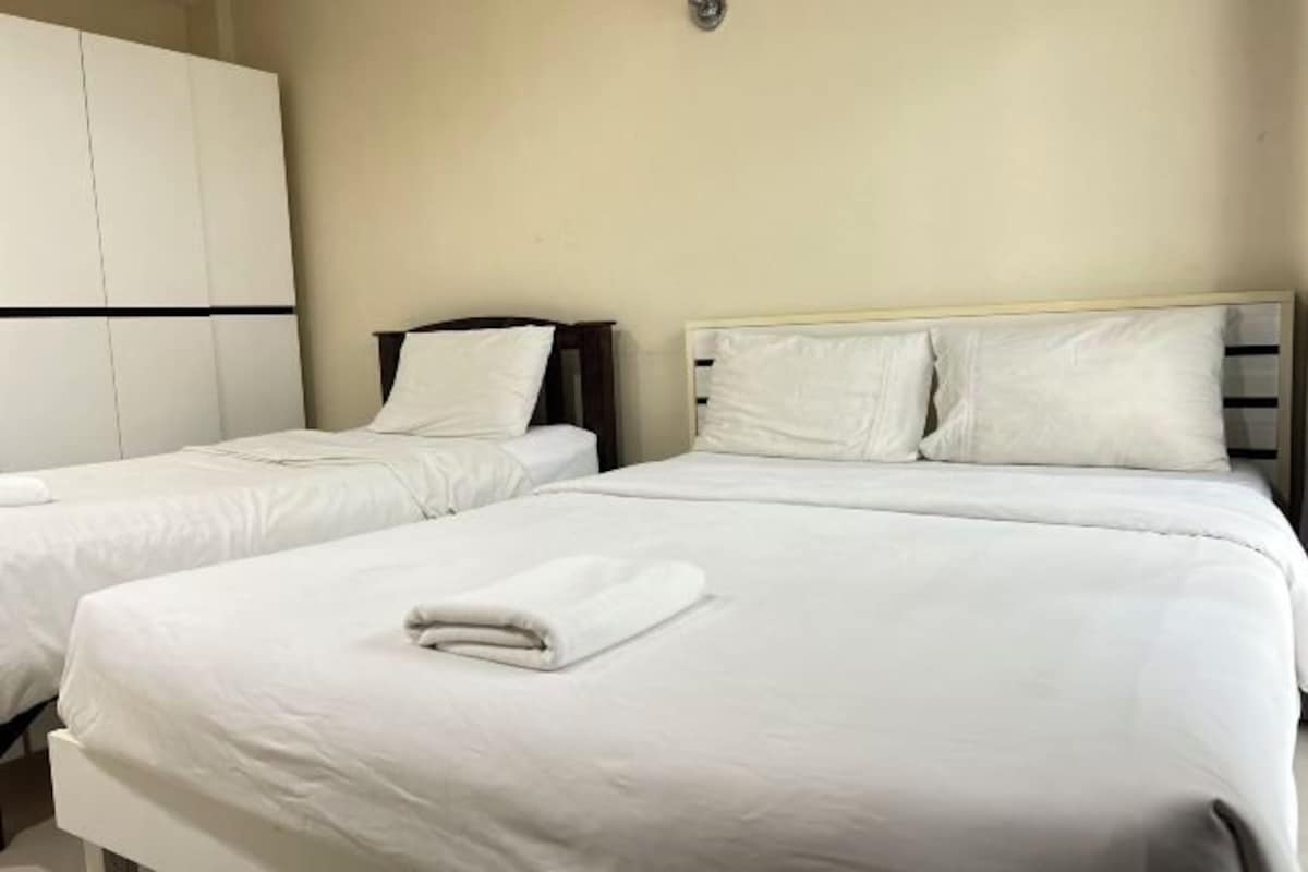 A hotel room with two single beds, each with white bedding and pillows, and a large wardrobe with a black stripe.