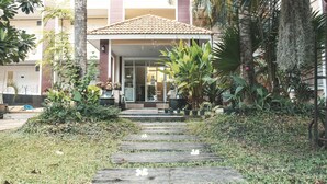 A building with a tiled roof, a covered entrance, and a garden with various plants and a wooden pathway leading to the entrance. - Nattida Place (Chiang Mai)
