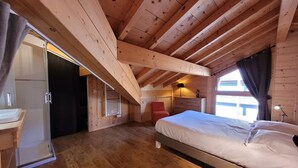 A wooden cabin bedroom with a bed, a chair, a desk, and a window with curtains. - Spacious apartment in village center with parking (Les Gets)