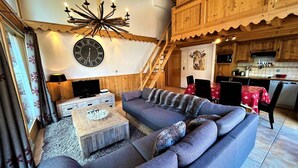 A cozy living room with a large sectional sofa, a wooden coffee table, and a wall-mounted clock. - Spacious apartment in village center with parking (Les Gets)