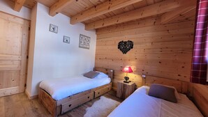 A cozy wooden room with two beds, a small table with a lamp, and a heart-shaped decoration on the wall. - Spacious apartment in village center with parking (Les Gets)