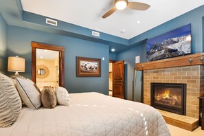 A bedroom with a large bed, a fireplace, a ceiling fan, and a painting of a mountain scene. - Silver Star 4303 | Penthouse | Hot Tub (Park City)