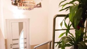 Un escalier avec une rampe métallique, une porte dotée d’un panneau de verre et un pot de fleurs orné de fleurs rouges.