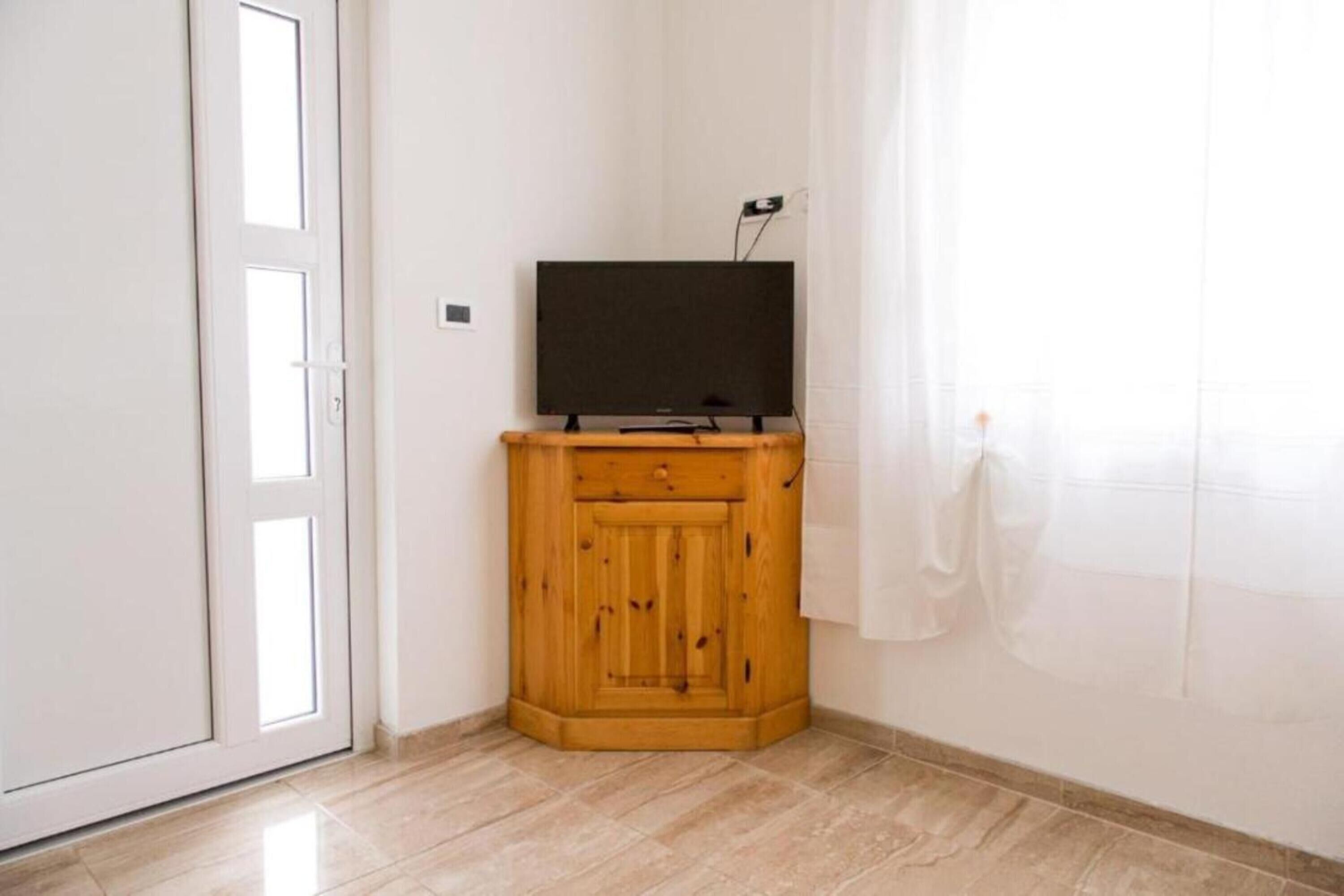 A corner room with a wooden cabinet, a television on top, and a door with a window.