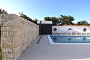 A swimming pool with a stone wall and a tiled deck. - Nada Apartmani (Pula)