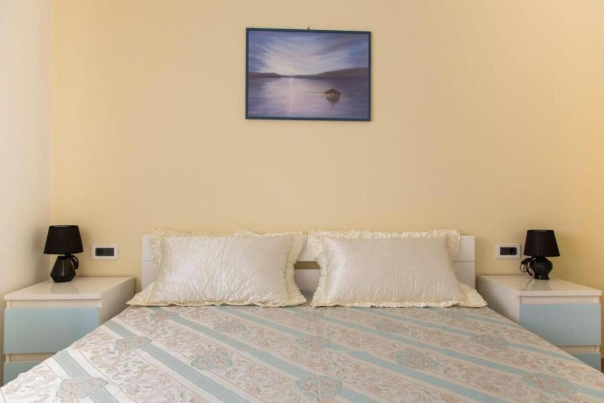 A bedroom with a bed, two nightstands, two lamps, and a painting of a landscape.