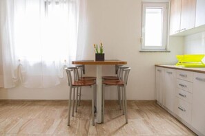 A kitchen with a dining table, chairs, a potted plant, and a window. - Nada Apartmani (Pula)