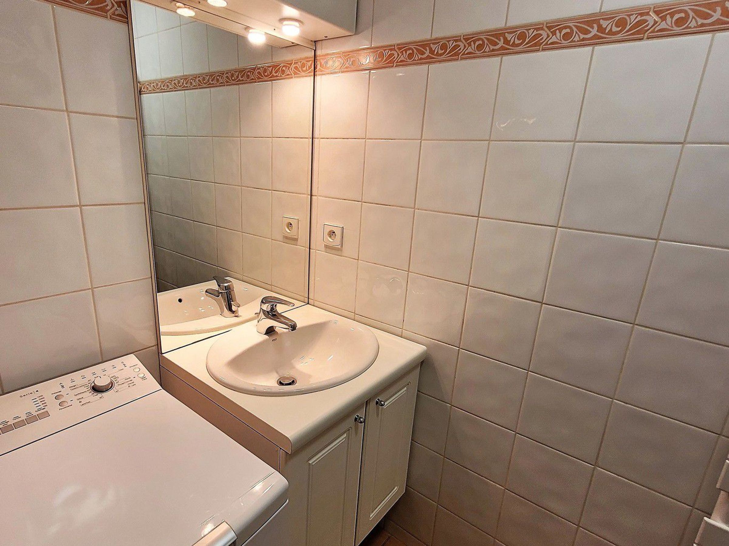 A bathroom with a white sink, a mirror, and a wall-mounted light fixture.