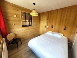 A wooden-paneled room with a bed, a chair, a window, and a door.