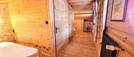 A wooden cabin interior with a single bed, a wardrobe, and a radiator.