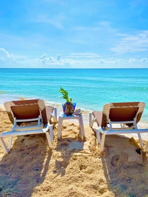 Two beach chairs facing the ocean with a small table between them, a decorative vase, and a seashell.