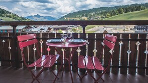 En balkon med et bord dækket til to, med udsigt over et bjergrigt landskab.
