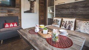 En hyggelig stue med træloft, et ophængt tv, en sofa med røde puder, et sofabord med en glasvase og en skål, samt en væg med et billede af et dyr.