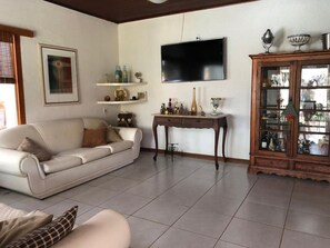 A living room with a sofa, a television mounted on the wall, a cabinet with glass doors, and a tiled floor. - Pousada Gente Bonita (Búzios)