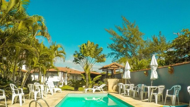 Una piscina con sillones de descanso y sombrillas, rodeada de palmeras y un cielo despejado.