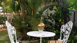 Una mesa metálica blanca con dos sillas, cada una con un cojín a rayas, en un jardín con palmeras y una valla blanca.